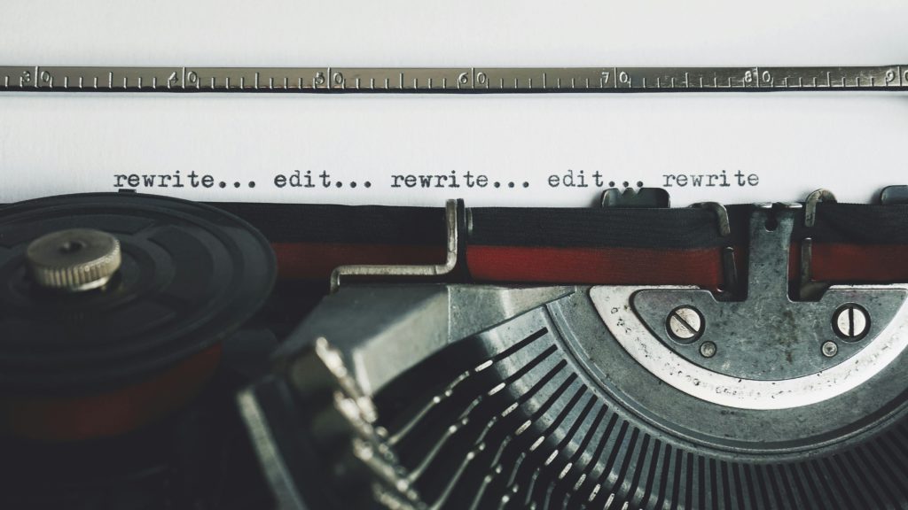 The difference between writing for the media vs. writing a novel. Photo of a typewriter up close saying 'rewrite...edit...rewrite...edit...rewrite'