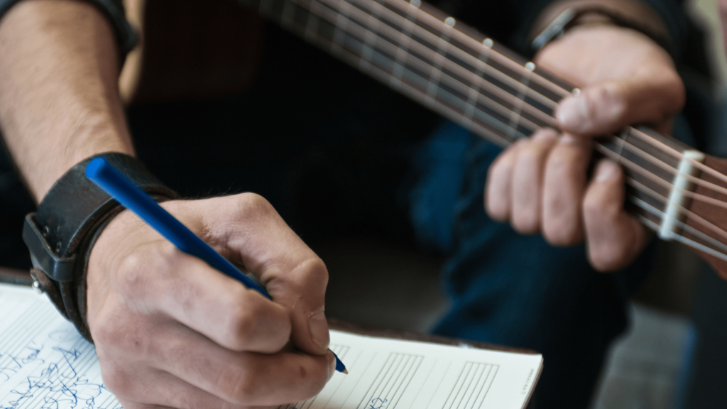 Songwriting prompts for when you're stuck. Photo of a person writing music holding their guitar.
