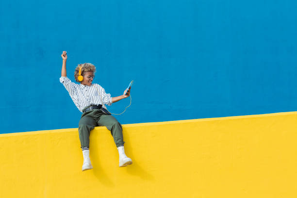 What does 'remastered' mean in music? Photo of a person sat on a yellow wall with a blue background. They are listening to music.