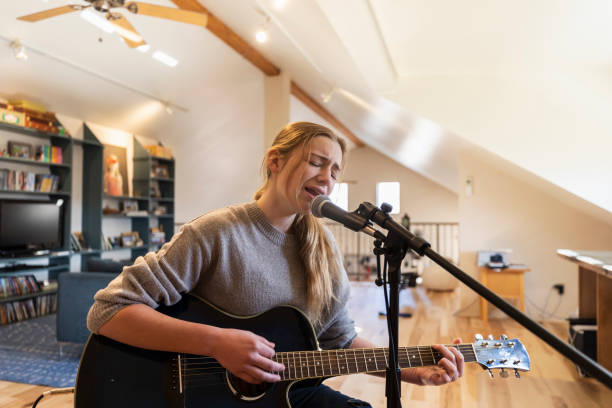 Recording without perfectionism: embracing the messy first draft. Photo of a girl singing into a microphone, playing the guitar at home.