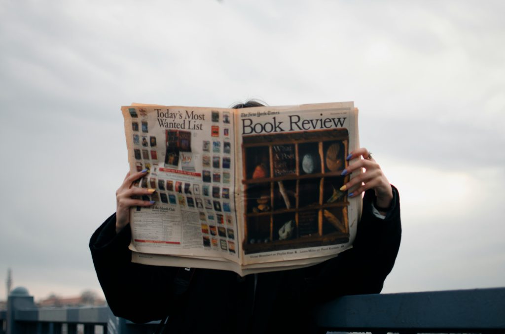 The art of writing headlines that make people click. Photo of someone hiding their face behind a newspaper.