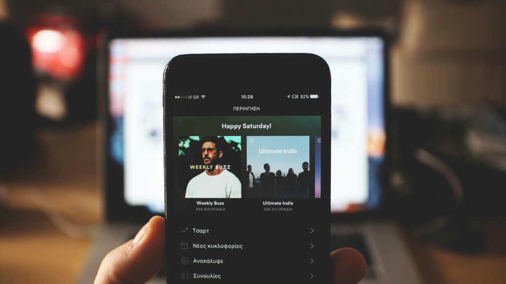 How to make a playlist go viral on Spotify. Photo of a smartphone in front of a laptop, the phone has Spotify loaded.