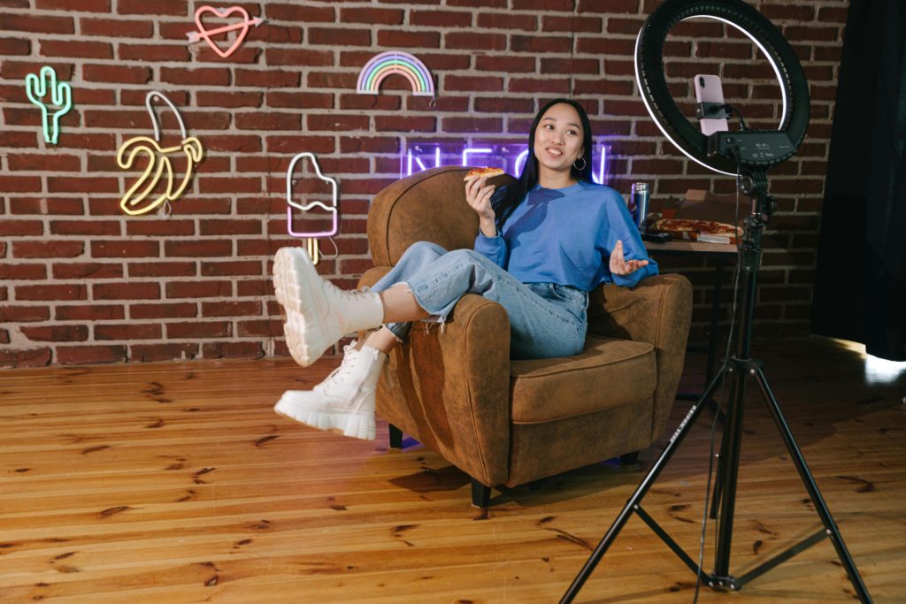 The 5 types of posts every small creator should be making. Photo of a girl sat on a chair talking into a smartphone which is on a ring light tripod.