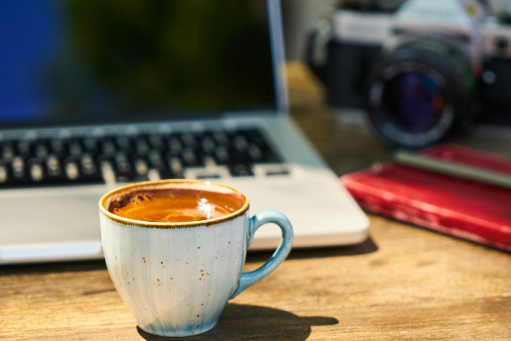 What a DIY press kit is and why every creator needs one. Photo of a coffee on the desk, behind is a laptop, a textbook and a camera.