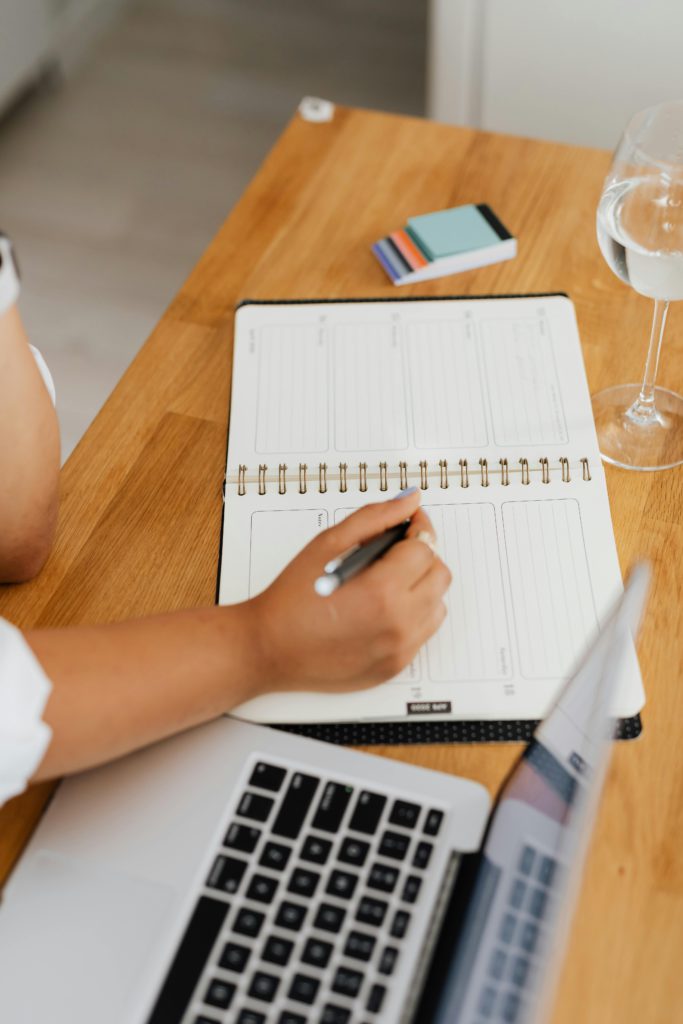 How to use social media to get booked for gigs, commissions, or collaborations. Photo of a person writing into a diary with a laptop next to them.