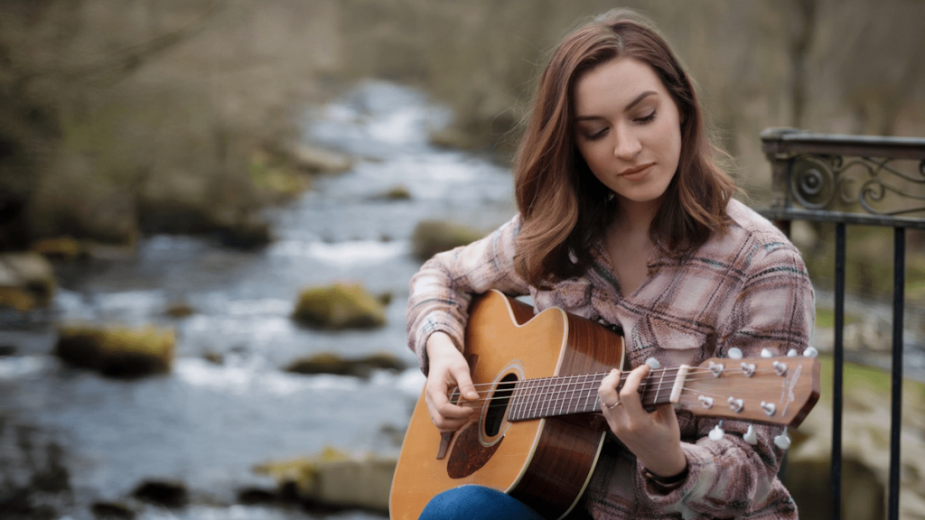 How to choose your artist name and branding (that fans will remember). Photo of a female artist playing guitar in front of a steam.