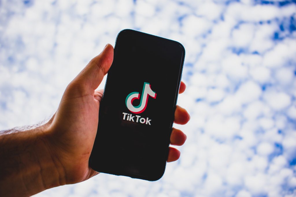 The TikTok-ification of songwriting: How the 15-second hook is rewriting the rules of pop. Photo of a hand holding a phone with TikTok loaded on the screen, against a cloudy background.